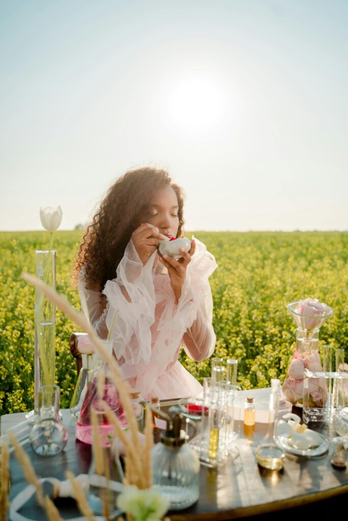 Woman with curly hair smelling perfume in a flower field during a sunny day.